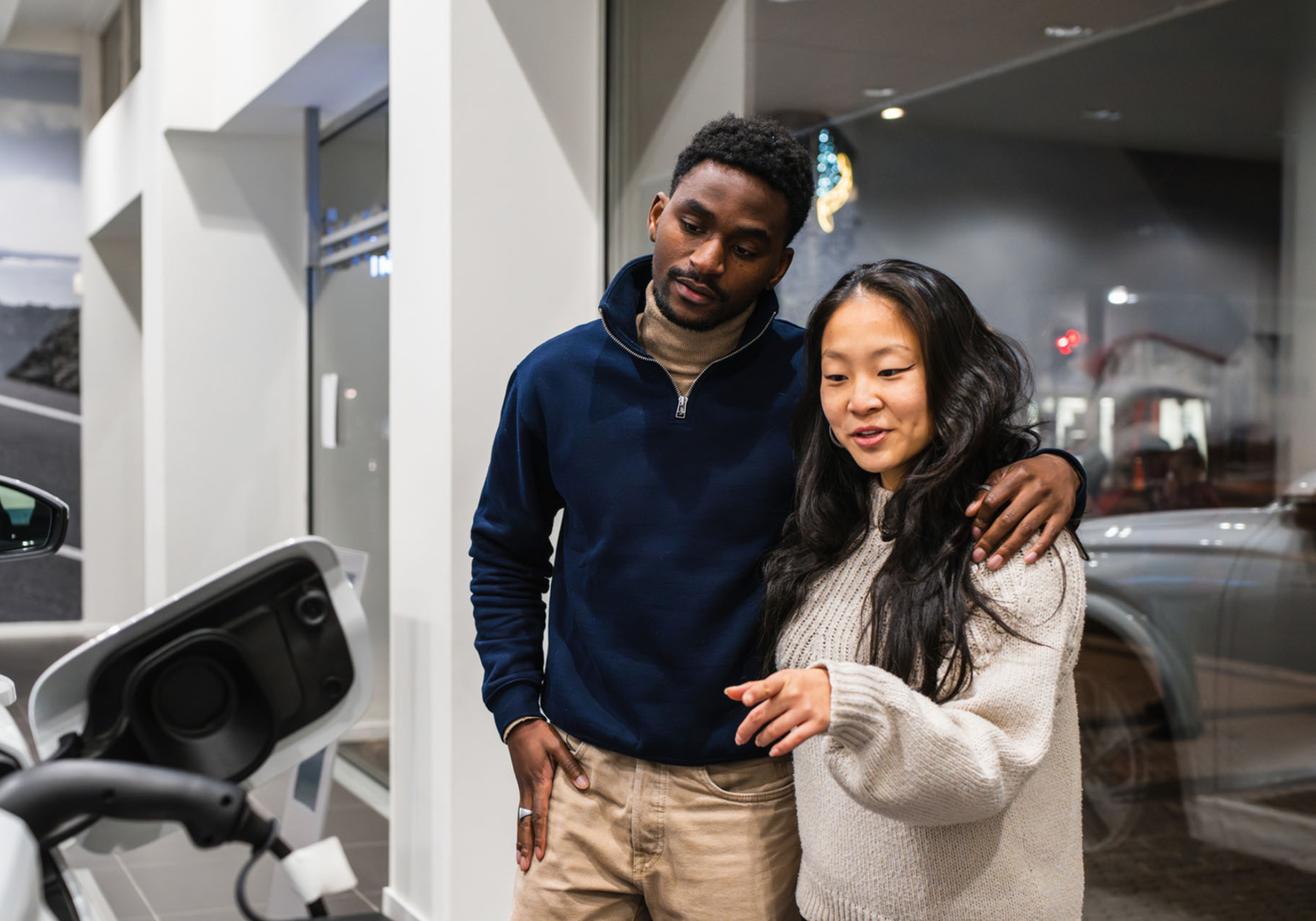 A couple shopping for an electric car at a dealership, examining a vehicle.